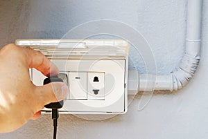Close up left hand of man is holding black plug and prepare for battery charging a mobile phone on the electric socket on the gray