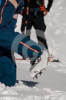 Close-up of leg of man with climbing crampons over mountaineering shoes for walking through glacier.