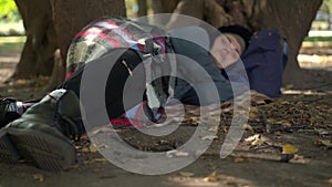 Close-up legs of blurred homeless young woman sleeping under the tree in urban park. Exhausted tired Caucasian tramp