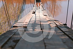 Close-up legs of family mom, dad and daughter walk on the old suspension bridge over the river.