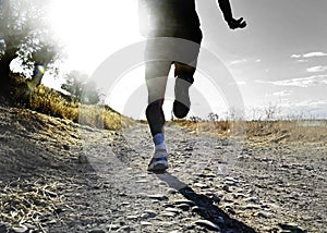 Close up legs and feet of extreme cross country man running and training on rural track jogging at sunset