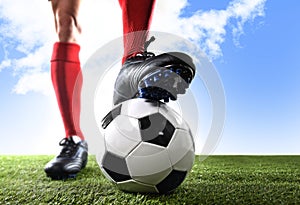 Close up legs feet football player in red shocks and black shoes posing with ball standing on grass outdoors