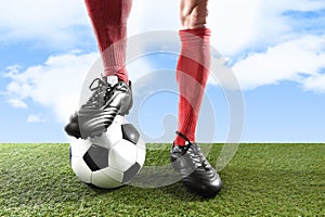 Close up legs feet football player in red socks and black shoes playing with ball on grass pitch outdoors