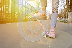 Close-up legs girl skateboarder blue jeans and pink sneakers riding pink penny skate longboard.