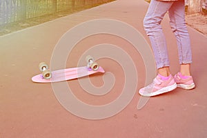 Close-up legs girl skateboarder blue jeans and pink sneakers riding pink penny skate longboard. Concept of sports
