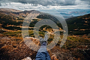 Close up legs in hikking shoes sitting on edge of mountains