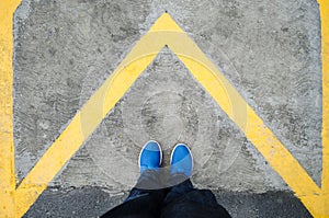 Close up on the legs of a man standing on a yellow triangle in the shape of an arrow, man standing on an arrow in a forward direct