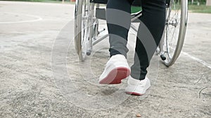 Close-up Legs of Mother pushing daughter in wheelchair relaxing on the road in the park. Disabled, childhood concept.