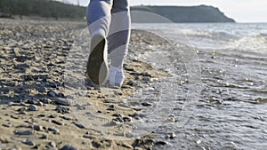 Close-up of the legs of a runner running along the beach and dodging the waves