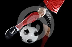 Close up legs and soccer shoe of football player in action kicking ball isolated on black background