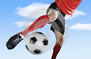 Close up legs and soccer shoe of football player in action outdoors kicking ball isolated on blue sky