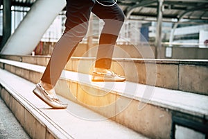 Close up legs of traveling people walking on stepping up stair in modern city. Sneakers and jeans elements. Business and travel