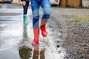 Close-up of legs of two kids boys wearing red and green rain boots and walking during sleet and rain on rainy cloudy day