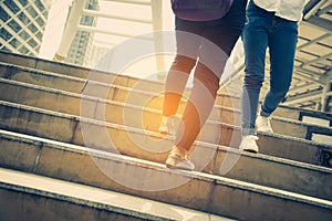 Close up legs of two traveling people walking on stepping up stair in modern city. Sneakers and jeans elements. Business and