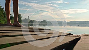 Close-up of legs of a woman in blue dress step on a wooden pier on sunny summer day. Girl feet walk along the dock. Lake