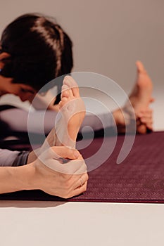 Close-up legs of a woman doing yoga while sitting on a light background. Athletic woman stretches on a mat in the studio