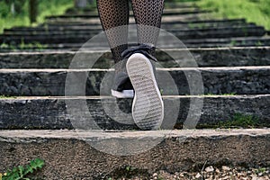 Close up of the legs of a woman in stockings with sneakers climbing the stairs in the nature