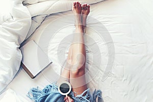 Close up legs women on white bed. Women reading book and drinking coffee in morning relax mood in winter season.