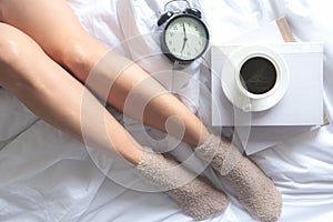 Close up legs women on white bed.  Women reading book and  drinking  coffee in morning relax mood in winter season.