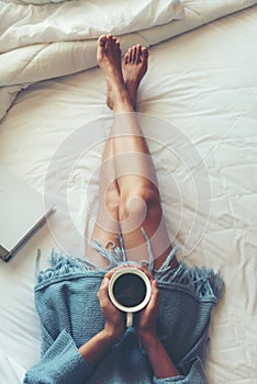 Close up legs women on white bed. Women reading book and drinking coffee in morning relax mood in winter season