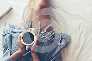 Close up legs women on white bed in the bedroom. Women reading book and drinking coffee in morning relax mood in winter season.