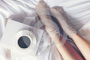 Close up legs women on white bed. Women reading book and drinking coffee in morning relax mood in winter season.