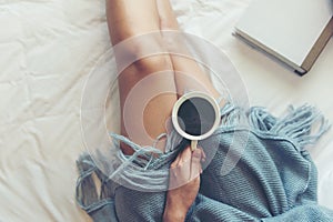 Close up legs women on white bed. Women reading book and drinking coffee in morning relax mood in winter season.