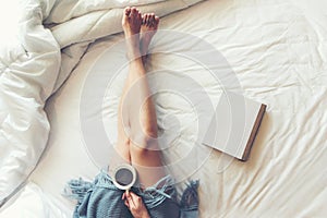 Close up legs women on white bed. Women reading book and drinking coffee in morning relax mood in winter season