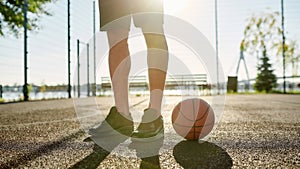 Close up of legs of young basketball player in sportswear standing on the court with basketball on a sunny day