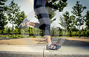 Close up legs of young man running in city park with trees on summer training session practicing sport healthy lifestyle concept