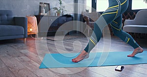 Close-up legs of young sporty woman doing lunge fitness exercises workout at home with smart phone on self isolation.