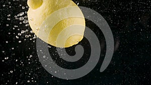 Close up of a lemon falling into water isolated on black background, slow motion. Action. Fresh yellow fruit moving