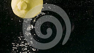 Close up of a lemon falling into water isolated on black background, slow motion. Action. Fresh yellow fruit moving