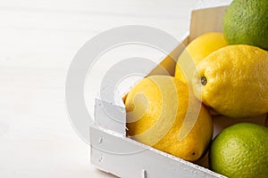 Close-up of lemons and limes in a white wooden box on white wood, with selective focus, horizontal