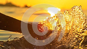 CLOSE UP: Young woman splashes water by dragging hand along the sea surface.