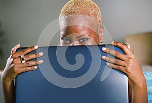 Close up lifestyle portrait of young classy attractive and happy black african american woman posing playful hiding behind laptop