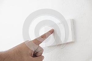 Close-up light switch of a male finger will turn on or off a light switch with white wall at home. white plastic mechanical switch