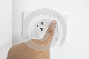 Close-up light switch of a male finger will turn on or off a light switch with white wall at home. white plastic mechanical switch