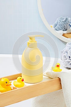 Close-up of a light yellow shower gel bottle displayed on a wooden tray with silicone ducks. Simulate bathroom space with body