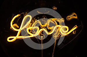 Close up of a lightbulb on dark background with bright wire in shape of the word Love