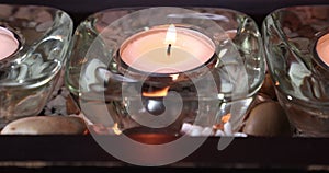 Close-up of lighting a tea candle with a match in glass candle holder, between two other candles