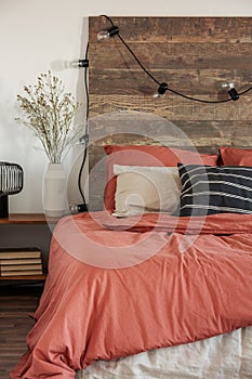 Close-up of lights hanging on a wooden bedhead in rustic bedroom interior with red sheets and black, striped pillow