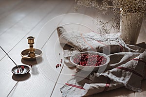 Close up of lingonberries in a bowl and linen tablecloth with some flowers, candlestick and incense on wooden table in bright