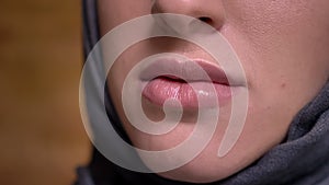 Close-up lip-portrait in profile of muslim woman in hijab smiling into camera on bricken wall background.