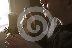 A close-up of lips at the microphone of a singing young man standing in profile in the rays of the sun