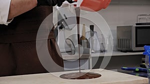 Close-up of liquid chocolate pouring on a wooden table in a modern pastry shop.