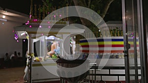 Close-up of lit incense sticks at night in Buddhist temple by Bodhi tree, enlightenment. Devotees practice rituals, seek