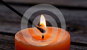 Close-up of a lit orange candle with matchstick igniting the wick