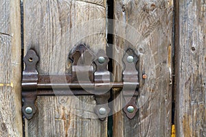 Close-up of lit by sun old rough made of wooden planks house door or barn gate with iron rusty slide bolt lock. Outdated technolog