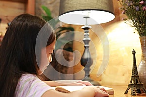 Close-up little Asian girl child in casual clothes reading a book and smiling on the desk in the room